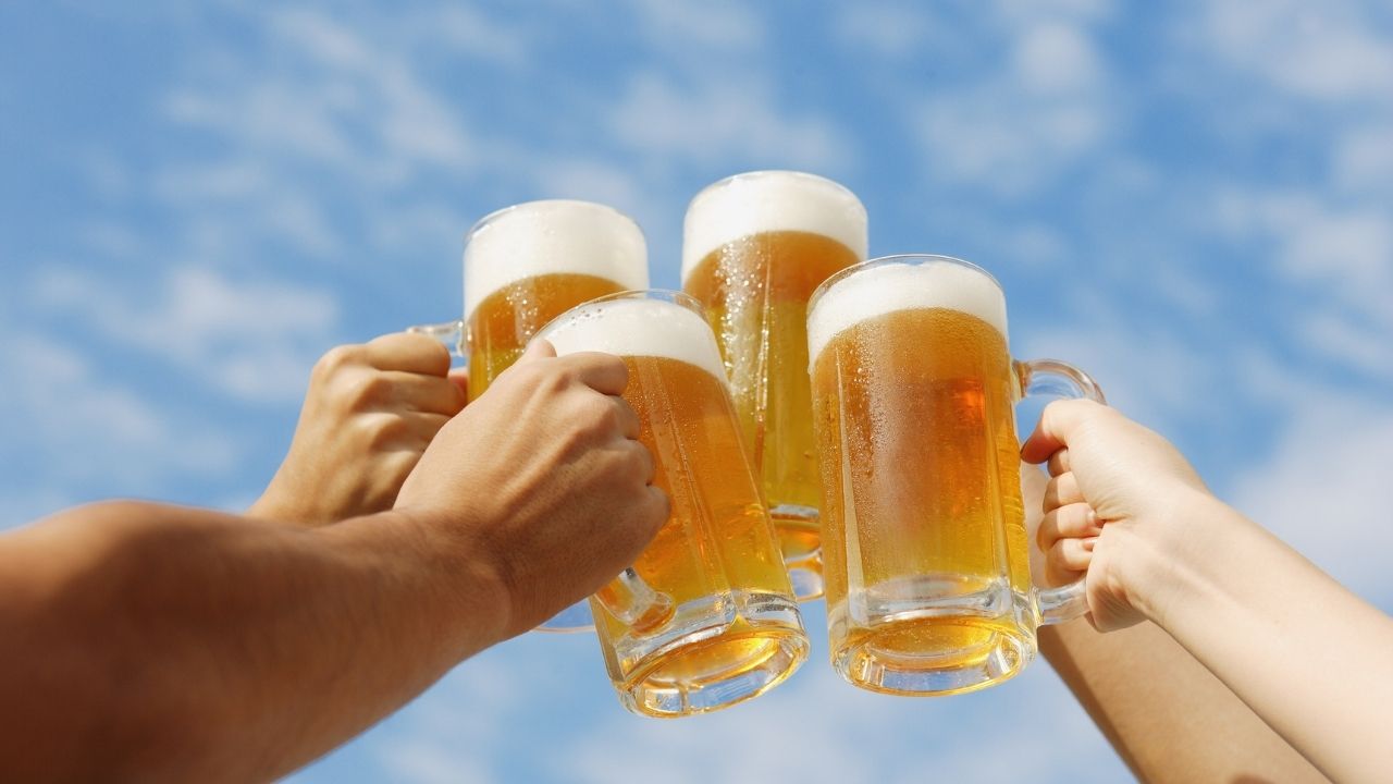 Four people cheers pint glasses of beer.