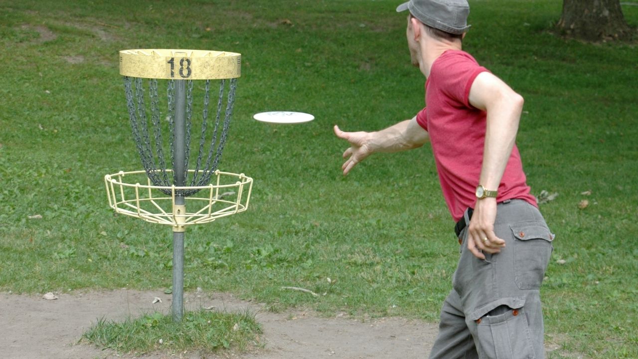 Man throws disc into disc golf net.
