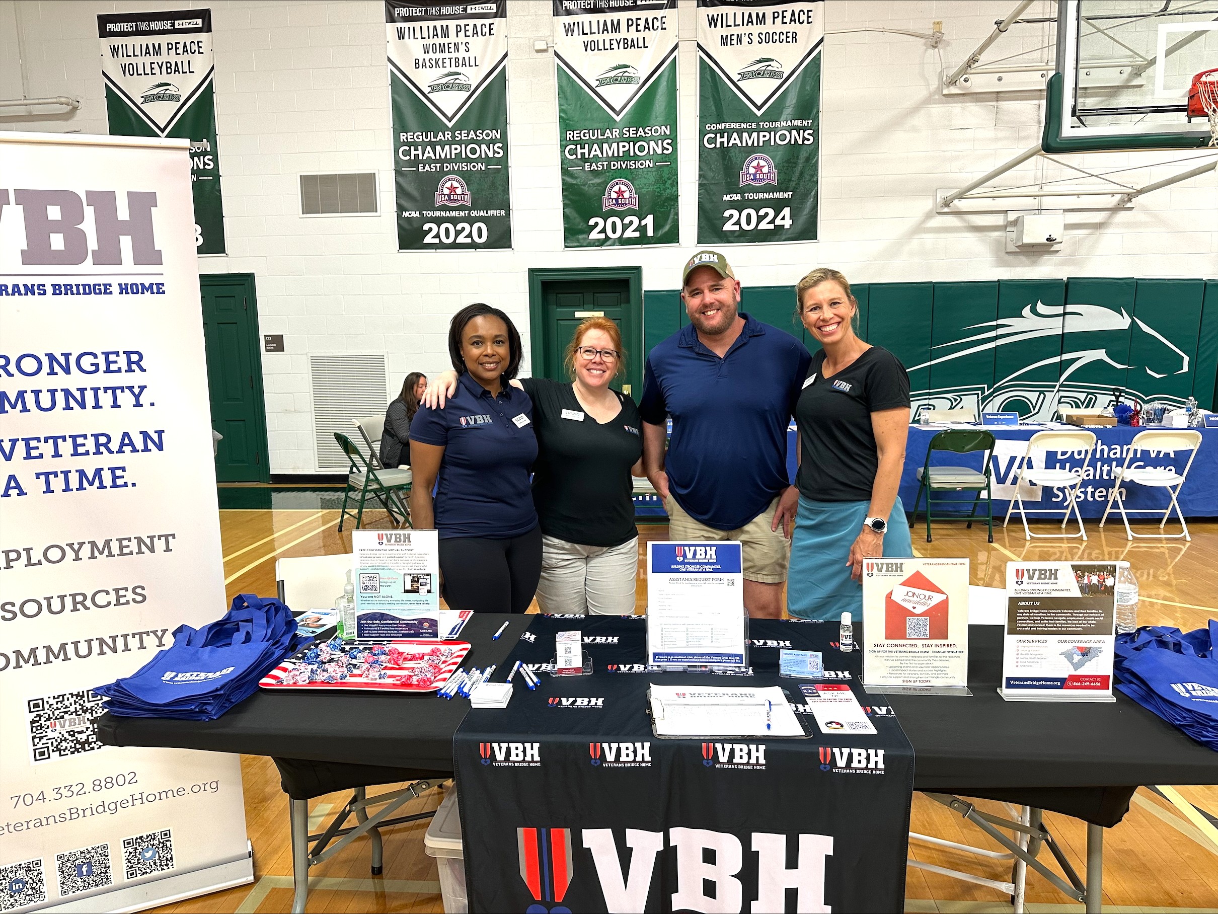 Four VBH-Triangle team members stand at VBH table welcoming veterans.
