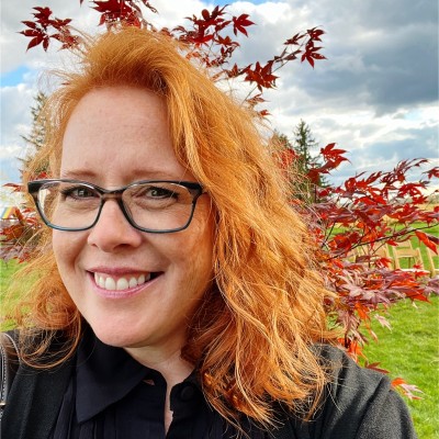 red haired woman smiling in front of tree with orange leaves