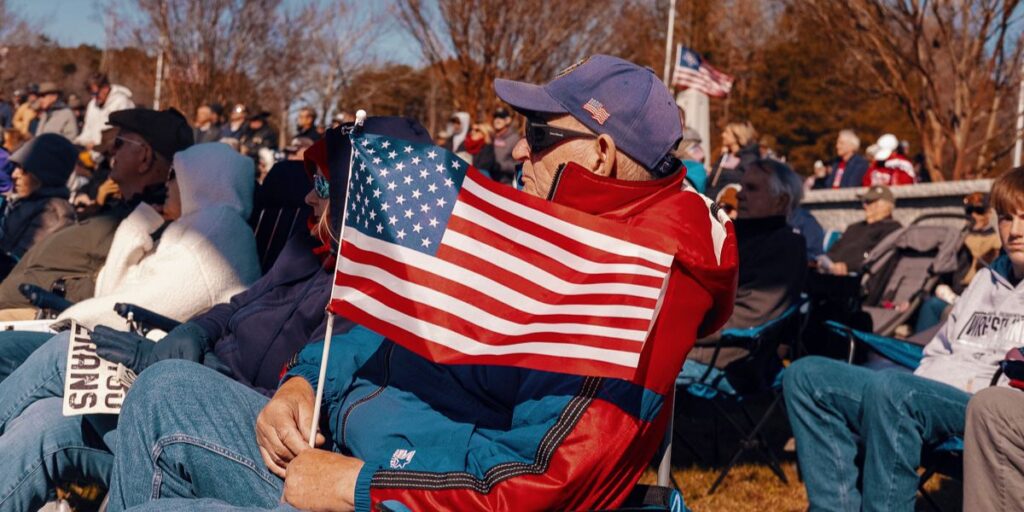 Older man faces the left and holds an American Flag