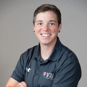 Professional headshot of a staff member smiling warmly, facing the camera against a clean, neutral background, dressed in business attire.